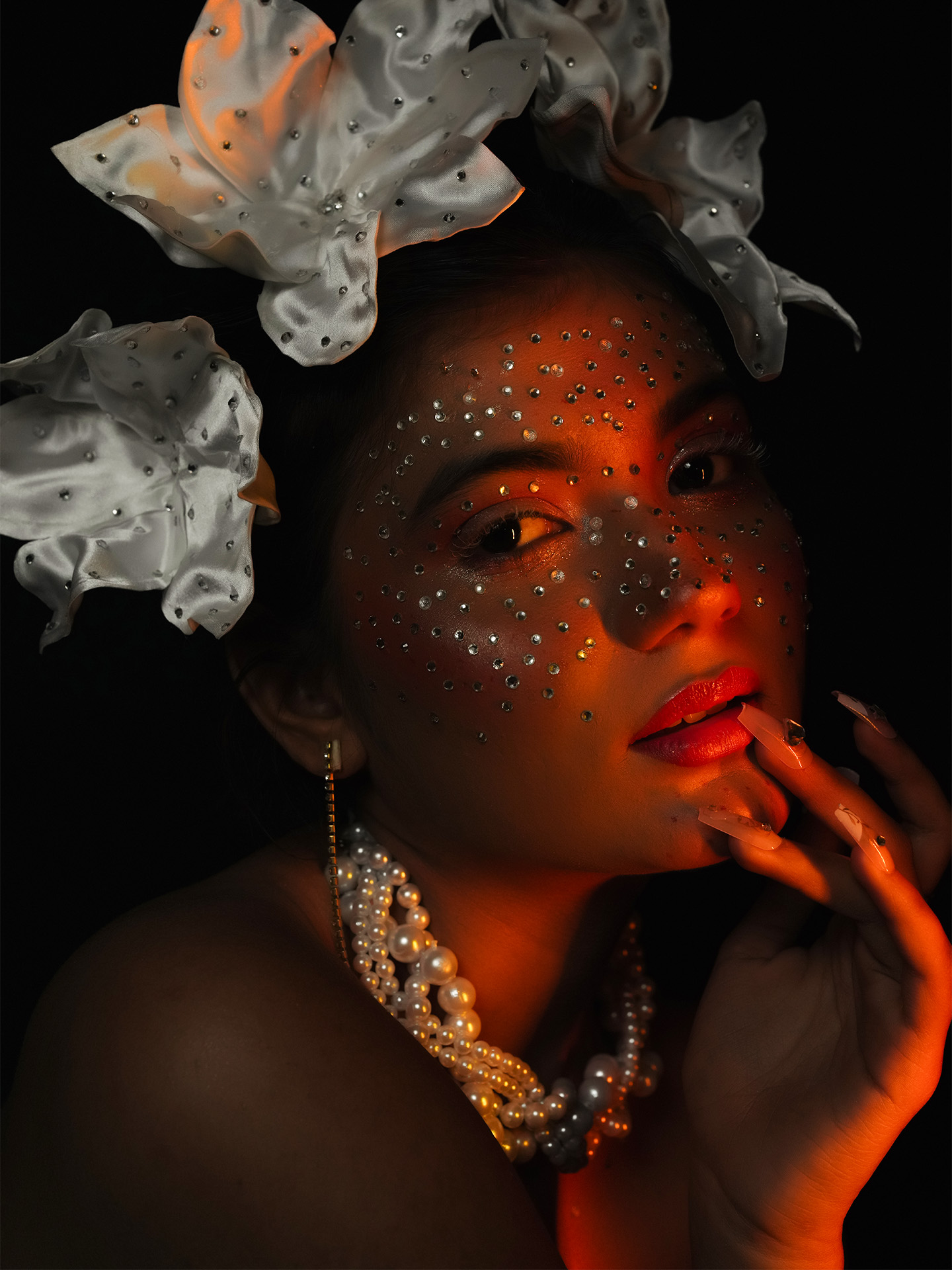 Editorial portrait — a model in amber light wearing pearls and white silk flowers